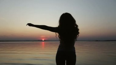 Arkadan bak. Genç bir kadın gün batımında dans ediyor..