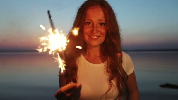 Junges Mädchen mit rotem Haar feiert Urlaub im Freien bei Sonnenuntergang und hält brennende Wunderkerzen in den Händen. — Stockvideo