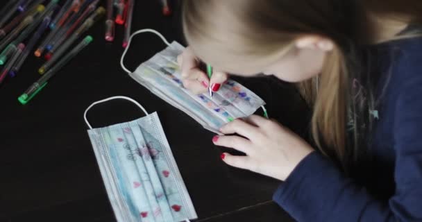 Das Kind zieht sich medizinische Schutzmasken über. Nettes Mädchen sitzt zu Hause. — Stockvideo