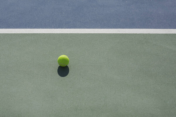 tennis ball on blue and green hard court divided with white line