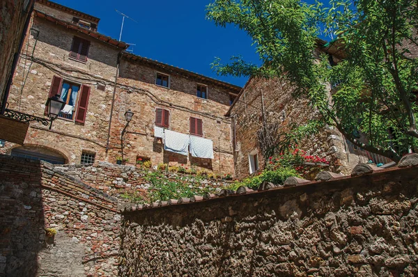 Vista da parede de pedra, edifícios antigos com plantas com flores e céu azul em Colle di Val d 'Elsa . — Fotografia de Stock