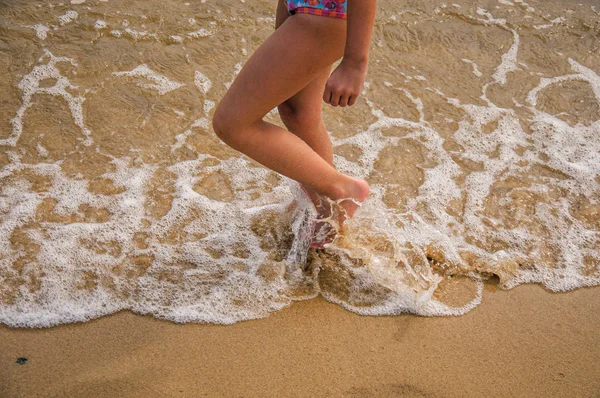 Close-up of child\'s legs walking on sand and sea water on beach near Paraty