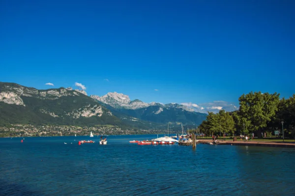 Vista do lago Annecy, com ilha, vegetação, barcos de remo, montanhas e céu azul no fundo — Fotografia de Stock