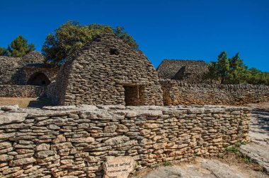 Taş duvarlı çit ve güneşli mavi gökyüzünde, kasaba Gordes yakınındaki Bories köyü ile yapılan tipik kulübe.