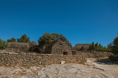 Taş duvarlı çit ve güneşli mavi gökyüzünde, Gordes yakınındaki Bories köyü ile yapılan tipik kulübe Panoraması.
