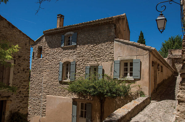 View of typical stone houses and wall with sunny blue sky, in alley of the historical city center of Gordes. Located in the Vaucluse department, Provence region, southeastern France