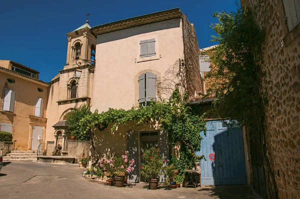 Hus med blommor och kyrkan med torn, framför ett torg i den historiska byn Lourmarin. — Stockfoto
