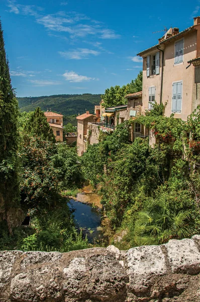 Vista de casas cerca de arroyo y acantilado con vegetación en el encantador pueblo de Moustiers-Sainte-Marie . — Foto de Stock