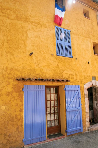 View of yellow house with blue blinds and flag, in the quiet and graceful village of Sillans-la-Cascade. — Stock Photo, Image