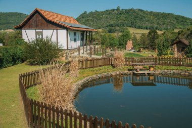 House and pond amid rural landscape clipart