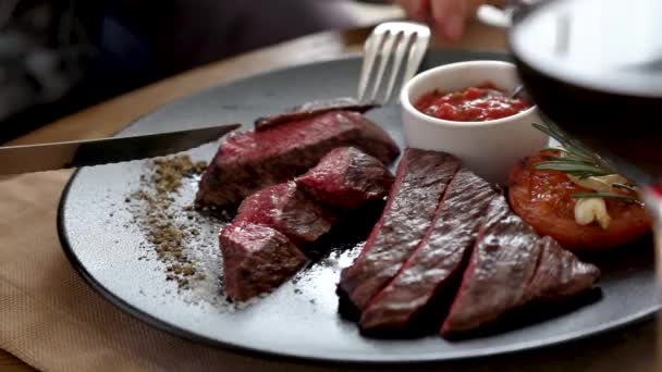 Mens handen gesneden steak. Voeg de saus toe aan het vlees. Op de voorgrond staat een glas rode wijn. — Stockvideo