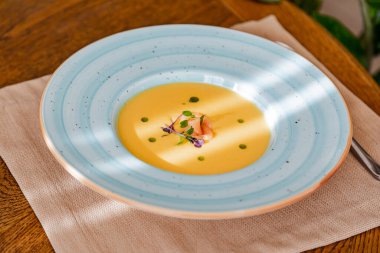 Somon balığı çorbası, parlak mavi bir tabakta, somon, mikroyeşillik ve tereyağıyla süslenmiş. Ahşap bir masanın arkasında..