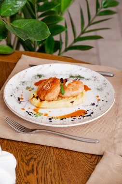 Güzel beyaz bir tabakta pirzola ile patates püresi. Tabak mikro-yeşilliklerle süslenmiş. İçerideki ahşap bir masanın arka planına karşı..