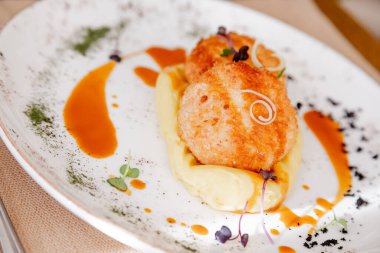 Güzel beyaz bir tabakta pirzola ile patates püresi. Tabak mikro-yeşilliklerle süslenmiş. İçerideki ahşap bir masanın arka planına karşı..