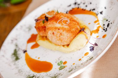 Güzel beyaz bir tabakta pirzola ile patates püresi. Tabak mikro-yeşilliklerle süslenmiş. İçerideki ahşap bir masanın arka planına karşı..