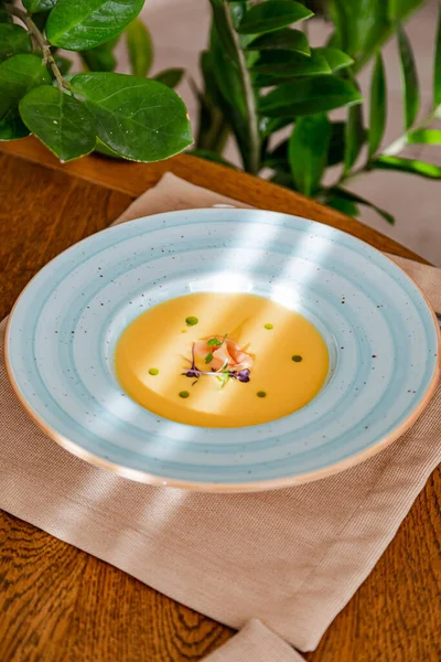 cream of salmon soup, in a bright blue plate, decorated with pieces of salmon, microgreens and butter. On the background of a wooden table.