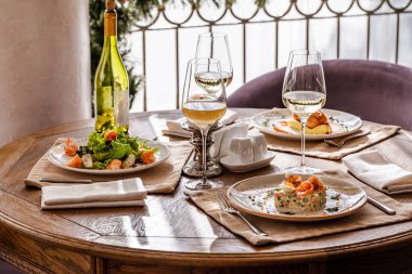 Tabaklarla servis edildi. Masanın üzerinde karides salatası, olivier salatası köfteli patates püresi ve İngiliz kahvaltısı var. Yemek için beyaz şarap servis edilir..