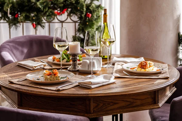 Mesa servida con platos. En la mesa hay ensalada de camarones, ensalada olivier, puré de papas con albóndigas y un desayuno inglés. El vino blanco se sirve para la comida . — Foto de Stock