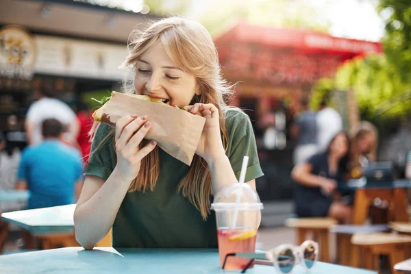 Gadis pirang yang lapar makan taco di food court pada hari musim panas yang cerah di taman . — Stok Foto