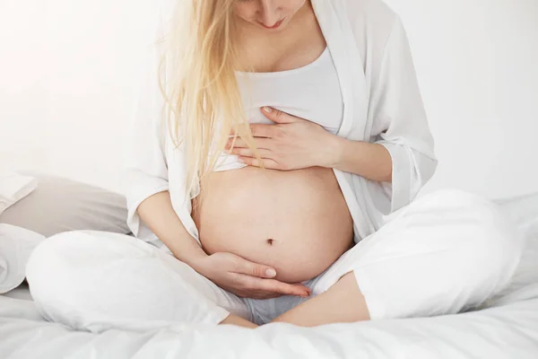 Mulher grávida loira olhando para a barriga e apoiando-a com as mãos esperando por seu menino ou menina para vir. Conceito de gravidez. Chave alta . — Fotografia de Stock