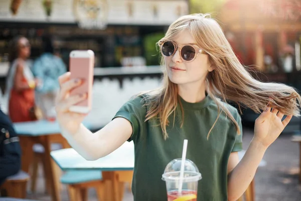 Blondes sommersprossiges Mädchen macht ein Selfie oder chattet per Videoanruf mit ihren Freunden, die an einem Sommertag im Park sitzen. — Stockfoto