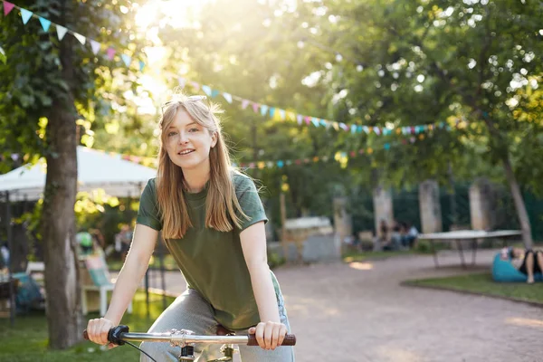 Блондинка їде на велосипеді. Портрет молодої скандинавської дівчини, яка катається на байку в міському парку, посміхається на камеру, дивлячись щасливим в зеленому кольорі в сонячний літній день. Концепція здорового способу життя . — стокове фото