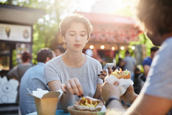 Pasangan makan kentang goreng dan burger pada hari musim panas yang cerah di taman pada faire memiliki waktu yang besar. Konsep makanan sampah . — Stok Foto
