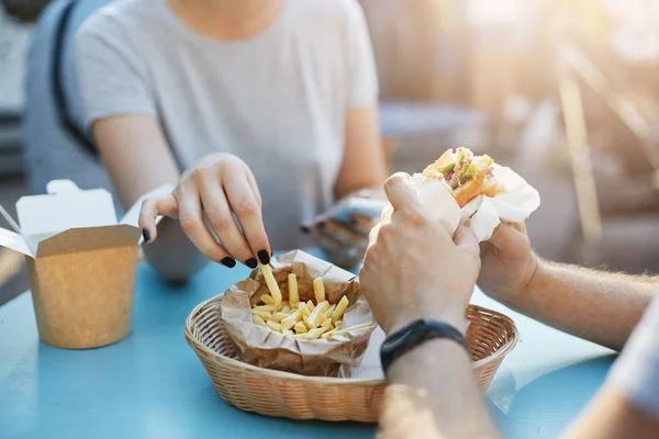 Menutup pasangan bahagia atau teman kerja memiliki burger dan kentang goreng selama makan siang di taman pada hari musim panas cerah chatting. Konsep makanan sampah . — Stok Foto