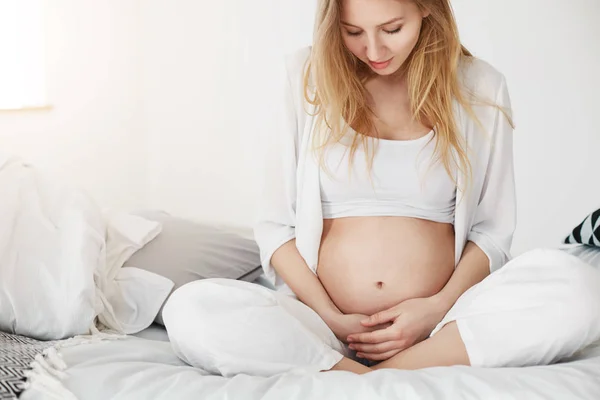 Mulher grávida relaxante em seu quarto desfrutando maternidade segurando sua barriga chutando . — Fotografia de Stock