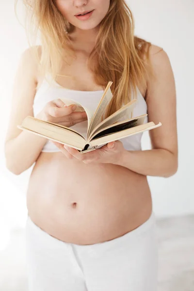 Close up de uma mulher grávida lendo um livro sobre bebês e família . — Fotografia de Stock