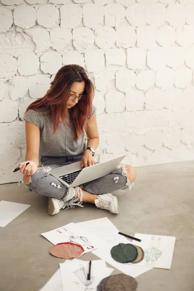 Perancang busana wanita bekerja pada laptop di studionya memeriksa kain dan sketsa duduk di lantai. Industri kreatif . — Stok Foto