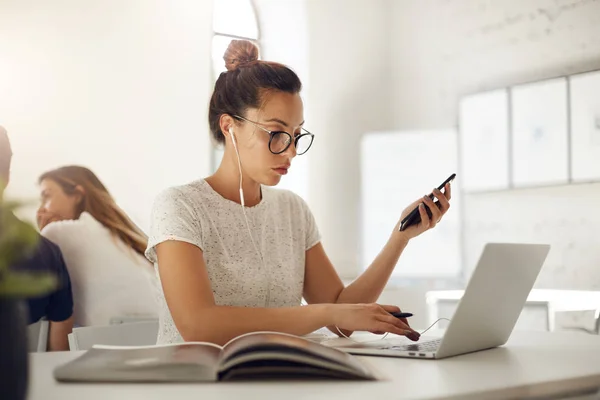 Modeontwerper zakenvrouw bezig met laptop surfen voor inspiratie in een heldere naaiatelier ruimte beluisteren online muziek met behulp van smartphone. — Stockfoto