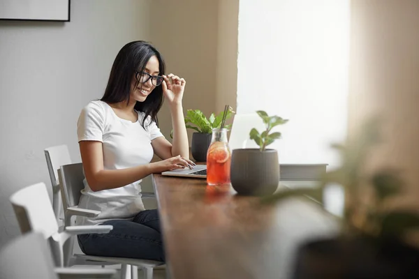 Joven estudiante asiático utilizando el ordenador portátil en la cafetería o coworking beber limonada sentado junto a una gran ventana. Concepto de estudio . — Foto de Stock