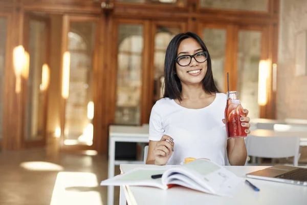 Giovane studentessa che si prende una pausa dalle lezioni seduta in un caffè usando il computer portatile e facendo i compiti a casa bevendo limonata. Concetto educativo . — Foto Stock