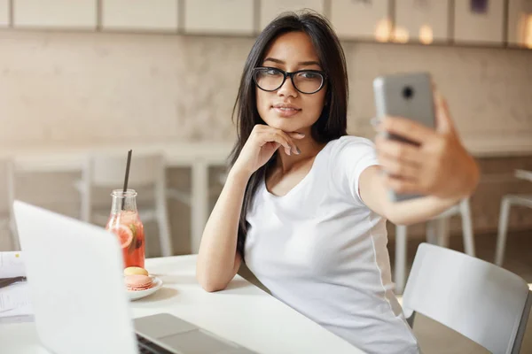 Frauen mögen sich selbst. junge asiatische Studentin macht ein Selfie im Café mit einem Handy, das ziemlich genial aussieht. — Stockfoto
