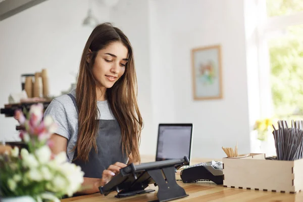 Bir ödeme terminal kullanarak bir kafe ve bir dizüstü bilgisayar çalışan genç kadın barista.