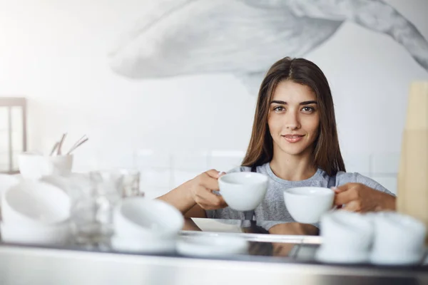 Barista perempuan memegang kopi dan cangkir teh untuk cappuccino siap untuk menempatkan mereka ke mesin espresso untuk menghangatkan mereka — Stok Foto