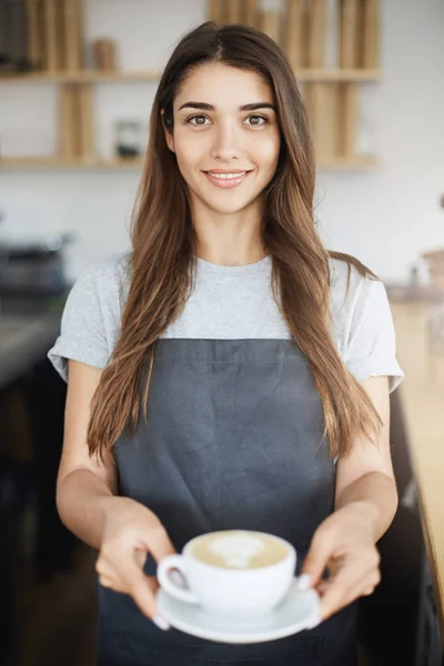 Coffee shop owner serving latte to her first visitor herself.