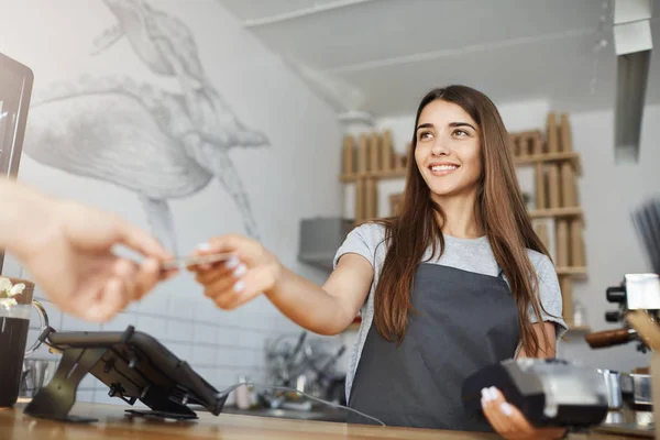 Kadın barista işlemek ve kredi kartı ödemeleri almak için bir banka terminal kullanarak müşteri ile etkileşim.