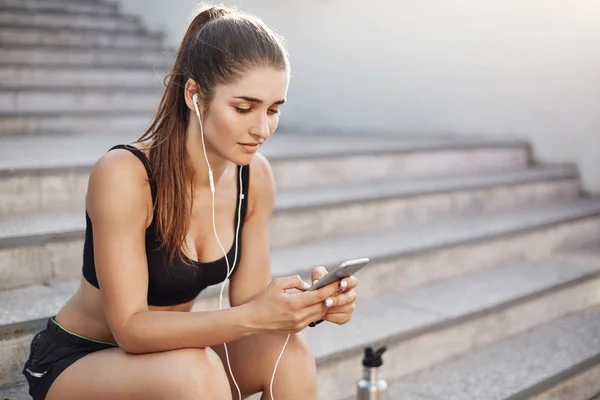 Female fitness trainer using a smart phone selecting music for her early morning workout in a busy city. Urban sport concept.