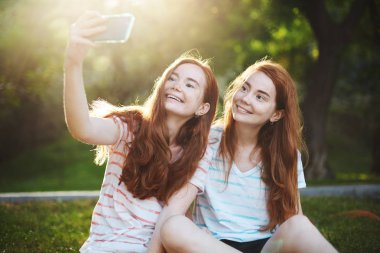 Sevinçli gülümseyen bir akıllı telefon, bir selfie alarak zencefil ikiz kız. Modern teknoloji insanlar her zamankinden daha çok bağlanır. Uzak bir arkadaşı çok eğlencelidir.