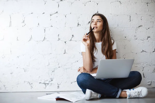 Young architect planning a public library renovation thinking of vistas. Female using laptop for her freelance work, sitting on floor concentrated.