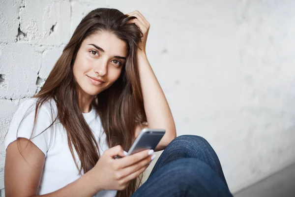 Potret wanita muda menggunakan ponsel sambil melihat kamera sambil tersenyum. Memperbarui profil jejaring sosialnya . — Stok Foto
