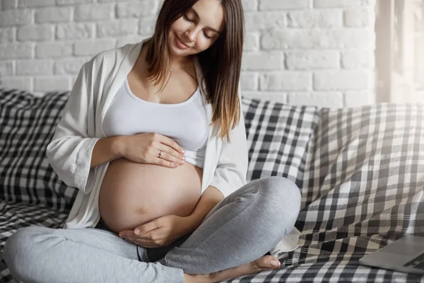 Linda senhora grávida cuidando de sua barriga ouvindo seu feto sentado em casa. Ter um marido rico é a chave para uma gravidez fácil . — Fotografia de Stock