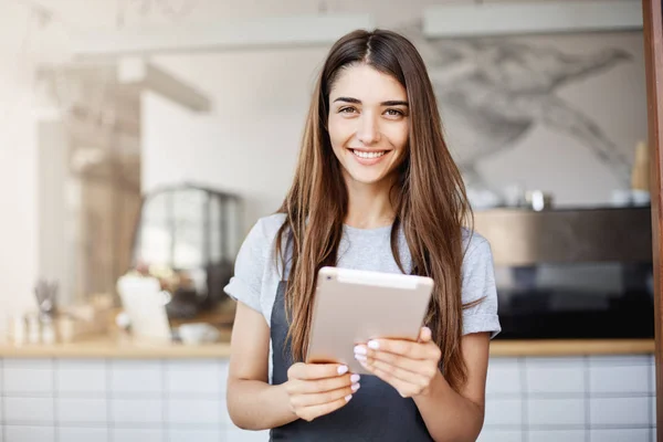 Gadis muda yang menggunakan komputer tablet yang menjalankan kafe sambil menatap kamera dengan gembira sambil menunggu pelanggan tersenyum . — Stok Foto