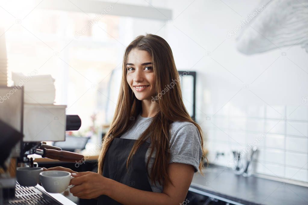 Sleepy young female starting her day on a new job as a barista. Looking happy and smiling at camera. Working in a cafe.