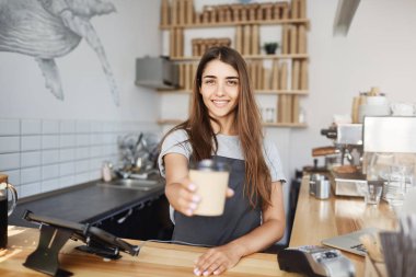 Genç kadın barista bir fincan cappucino veya geç kamera gülümseyen arayan müşteriye teslim. Bira harika tadı için taze kahve.