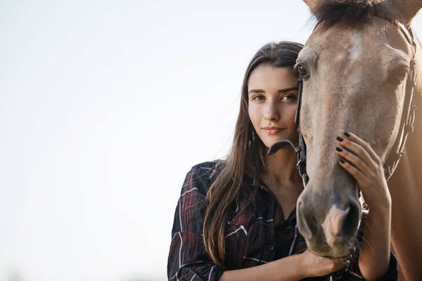 Retrato de uma jovem assistente de exploração agrícola segurando e acariciando um cavalo . — Fotografia de Stock