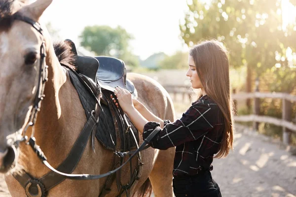 Młodych kobiet właściciel koni wiązanie dół siodło przygotowuje się przejechać aż do rzeki od zwierząt gospodarskich w słoneczny dzień jesień. — Zdjęcie stockowe