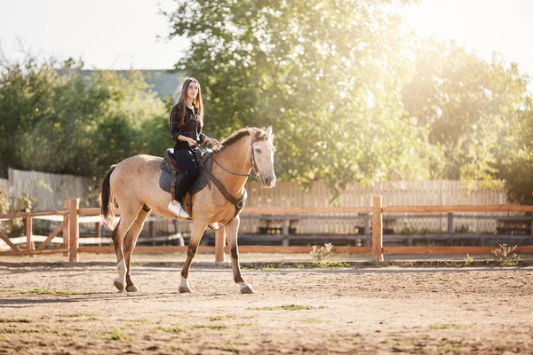 Young female farm manager riding a horse on a ranch on a sunny summer day.